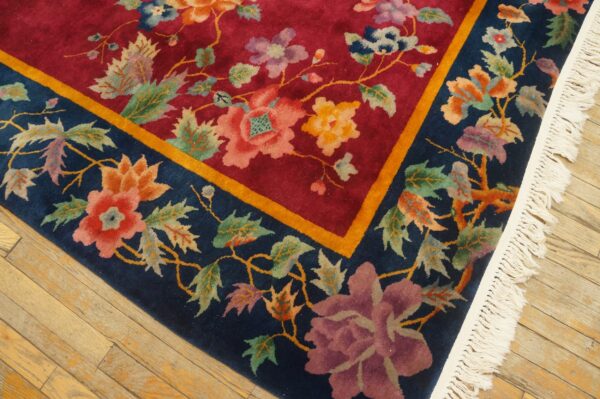 High-pile rug with red center and navy floral border accented by gold, visible on light wood flooring.