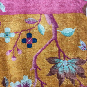 Plush rug detail featuring a gold field, pink border, and floral motifs in teal, magenta, and brown.