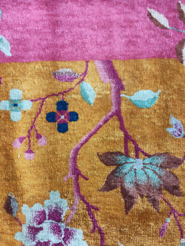 Plush rug detail featuring a gold field, pink border, and floral motifs in teal, magenta, and brown.