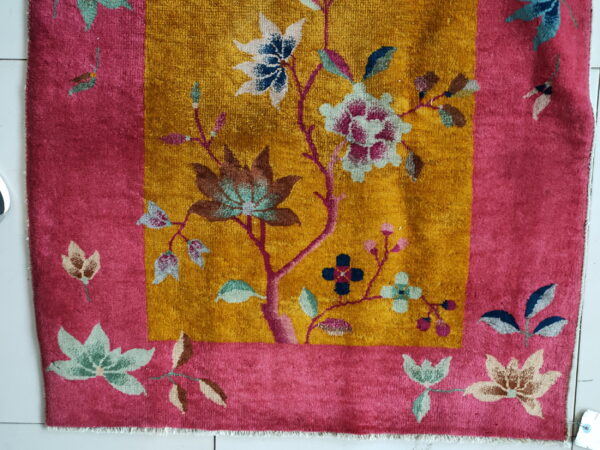 Golden yellow rug center with magenta border and multi-colored floral and leaf patterns on white tile.