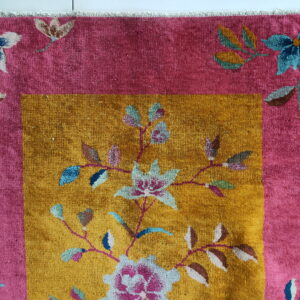 Close up of a high-pile rug with pink border and mustard yellow field featuring colorful floral patterns.