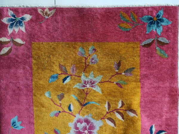 Close up of a high-pile rug with pink border and mustard yellow field featuring colorful floral patterns.
