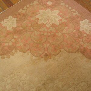 Close-up of a low-pile rug featuring a rose, tan, and cream floral pattern on visible wood flooring.