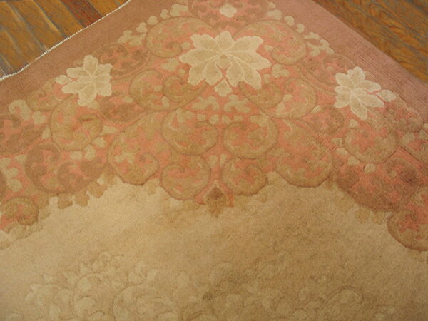 Close-up of a low-pile rug featuring a rose, tan, and cream floral pattern on visible wood flooring.