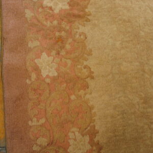Tan rug with a floral border in pink and cream next to worn wooden floorboards.