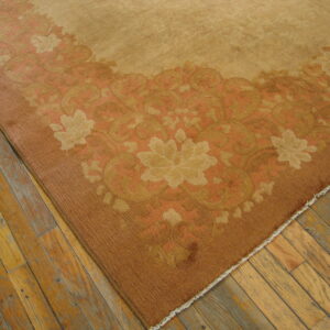 Low pile tan rug featuring a wide border of rust and gold floral motifs on distressed wood planks.