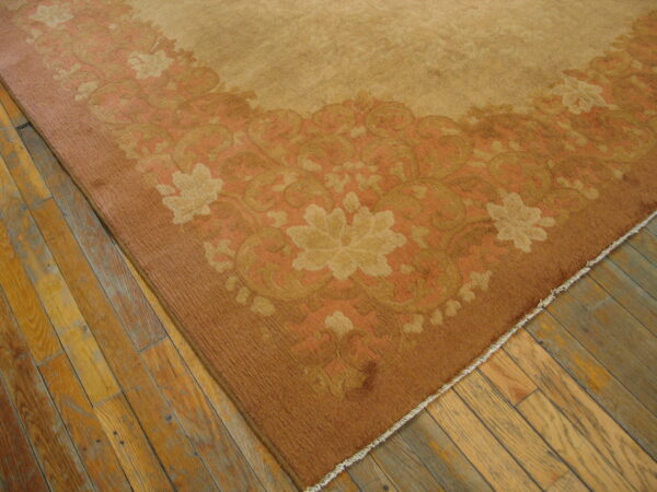 Low pile tan rug featuring a wide border of rust and gold floral motifs on distressed wood planks.