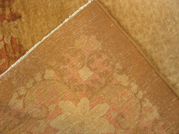 The corner of a plush gold and rust patterned rug is flipped to show the woven grid backing.