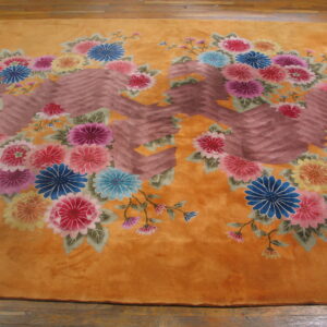 A high-pile golden rug with vivid floral bouquets and a brown chevron design is placed on wood floors.