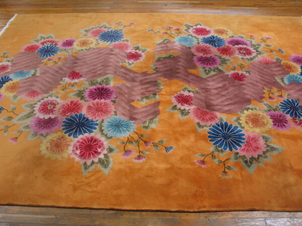 A high-pile golden rug with vivid floral bouquets and a brown chevron design is placed on wood floors.