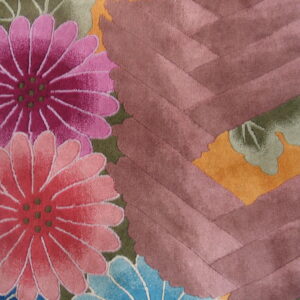 Close-up showing a cut-pile rug with pink, magenta, and blue flowers against green leaves and a mauve chevron pattern.