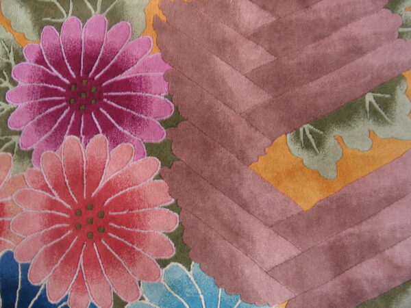 Close-up showing a cut-pile rug with pink, magenta, and blue flowers against green leaves and a mauve chevron pattern.
