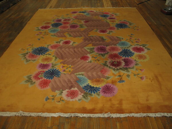 Yellow rug with large multicolored floral clusters and a prominent brown, zigzagging central motif on wood flooring.