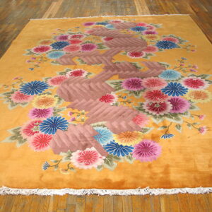 Plush orange rug displaying a dense bouquet of pink, blue, yellow, and red flowers on wood.