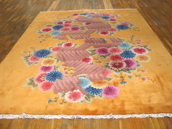 Plush orange rug displaying a dense bouquet of pink, blue, yellow, and red flowers on wood.