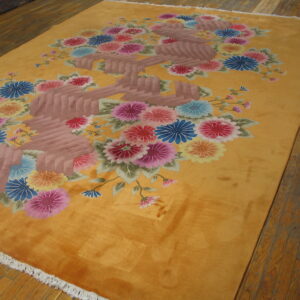 Vibrant golden rug featuring large stylized pink, blue, and yellow floral sprays on hardwood planks.