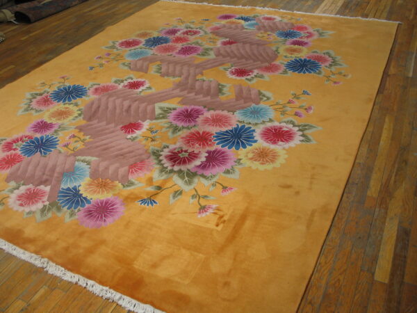 Vibrant golden rug featuring large stylized pink, blue, and yellow floral sprays on hardwood planks.