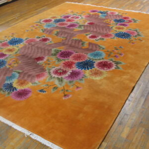 Orange floral rug featuring colorful pink, blue, and yellow blooms on a deep gold field over wood flooring.