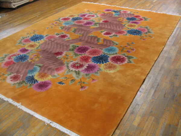 Orange floral rug featuring colorful pink, blue, and yellow blooms on a deep gold field over wood flooring.