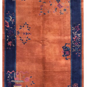 Rust-colored rug with a bold navy border displaying subtle stylized flowers and ornate vase motifs.