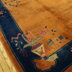 Rust orange rug with navy border and colorful floral vase pattern on light wood floor.