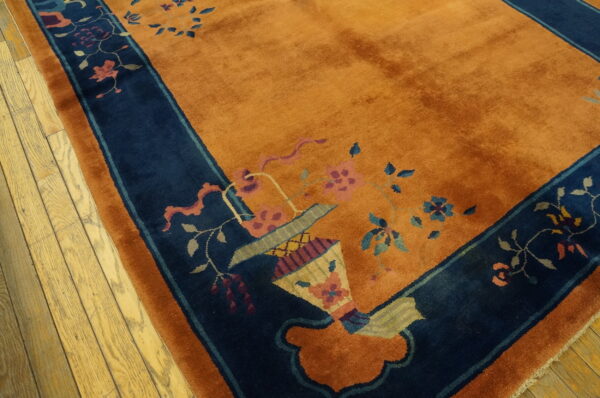 Rust orange rug with navy border and colorful floral vase pattern on light wood floor.