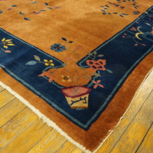Burnt orange rug with a navy blue border displaying colorful floral and vase motifs on wood flooring.