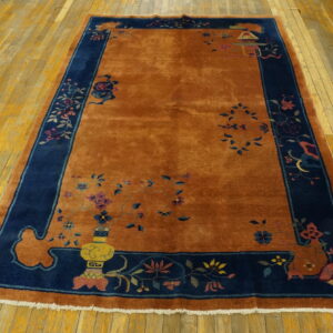 Plush orange rug with a navy blue border featuring multicolored floral and traditional decorative patterns on wood planks.