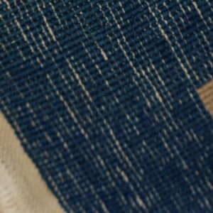 Flatweave rug detail featuring dark blue with white streaks, a cream border, and tan and yellow stripes.