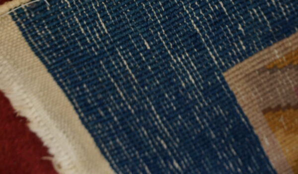 Flatweave rug detail featuring dark blue with white streaks, a cream border, and tan and yellow stripes.