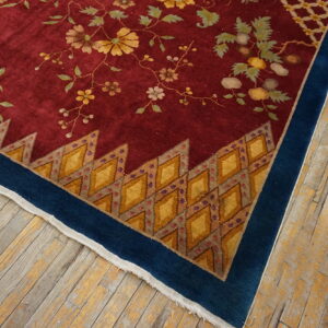 Maroon rug corner showing yellow vines, a jagged diamond inner border, and a solid blue outer border on worn wood floors.