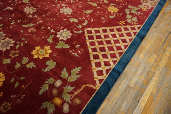 Burgundy rug detailed with yellow and white flowers, contrasting a blue border and rustic wooden floor.