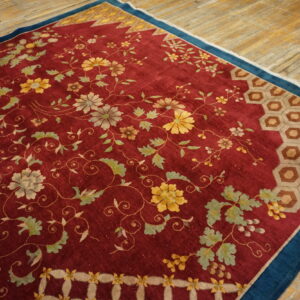 Low-pile red rug with detailed floral vines, honeycomb borders, and a dark blue edge resting on wood flooring.