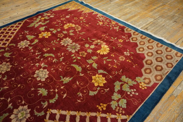 Low-pile red rug with detailed floral vines, honeycomb borders, and a dark blue edge resting on wood flooring.