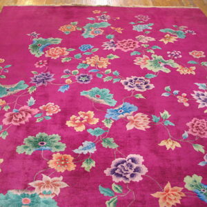 Magenta rug with a dense multicolored floral design displayed on light wooden floorboards.