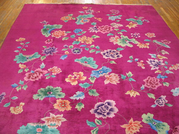 Magenta rug with a dense multicolored floral design displayed on light wooden floorboards.