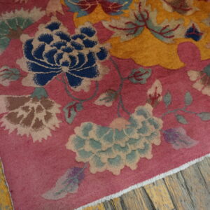 A rose floral rug featuring blue, mustard, and sage green motifs rests on distressed yellow wood planks.