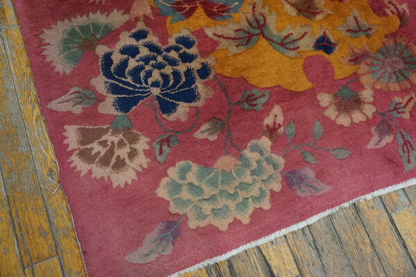 A rose floral rug featuring blue, mustard, and sage green motifs rests on distressed yellow wood planks.