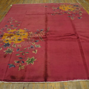 Rosy-red rug with large yellow and multicolored floral patterns displayed on light hardwood flooring.