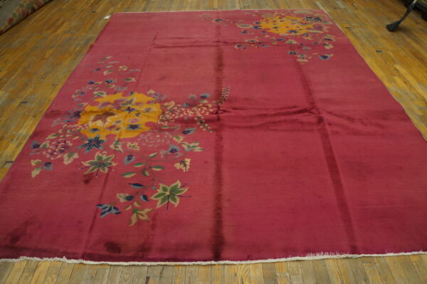 Rosy-red rug with large yellow and multicolored floral patterns displayed on light hardwood flooring.
