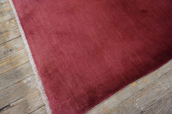 A deep red solid rug with visible pile variation rests on rustic gray wooden floorboards.