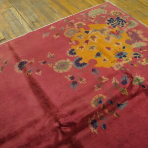 Deep rose rug with a golden central field and sprawling teal and green botanical patterns on distressed wood.