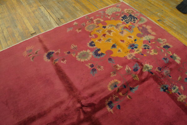 Deep rose rug with a golden central field and sprawling teal and green botanical patterns on distressed wood.