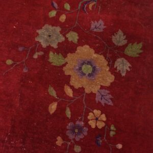 A deep red rug with a multicolored floral and vine pattern lies next to distressed light wood floorboards.