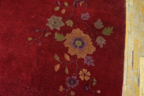 A deep red rug with a multicolored floral and vine pattern lies next to distressed light wood floorboards.