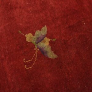 Deep red rug close-up showing a low pile and a gold, purple, and green butterfly motif.