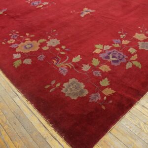 A deep red rug with a colorful floral and butterfly pattern rests on worn light-toned wood plank floors.