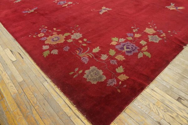 A deep red rug with a colorful floral and butterfly pattern rests on worn light-toned wood plank floors.