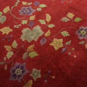 Deep red rug featuring an intricate scrolling floral vine pattern in shades of purple, gray, and olive green.
