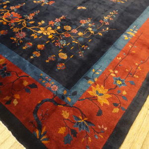 Ornate dark blue rug featuring multicolor floral branches and a wide rust red border on wood flooring.